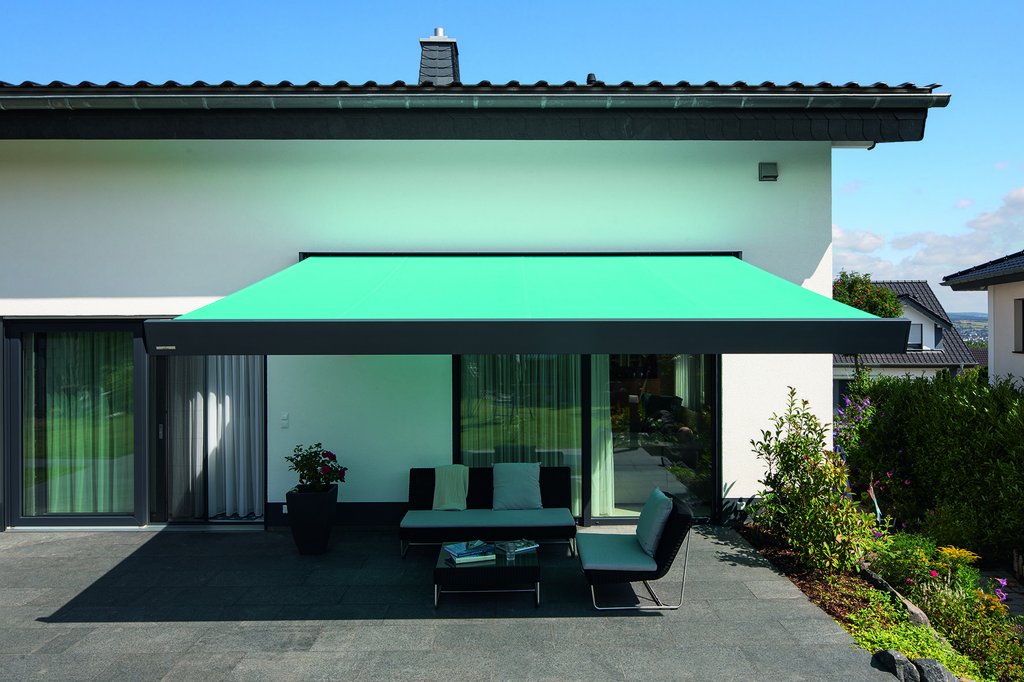 Eine grüne Markise überspannt einen Terrassenbereich vor einem modernen Haus.