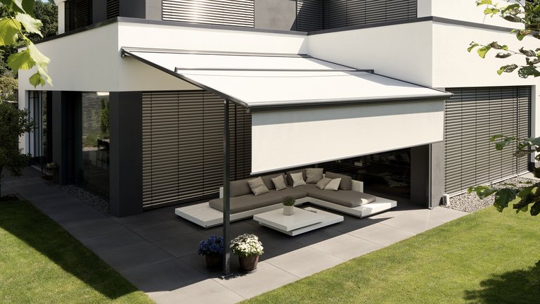 Eine helle Überdachung schützt eine moderne Terrassensituation mit Möbeln unter einem klaren Himmel.