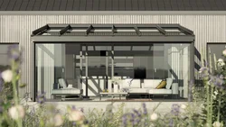 Moderne Hausfassade mit Glas-Schiebewänden und einer Überdachung, umgeben von bunten Blumen.