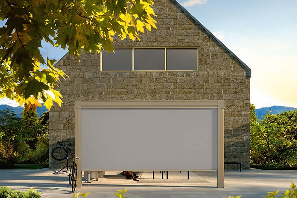 Haus mit grauer Fassade und Überdachung, im Vordergrund grüne Pflanzen und ein Fahrrad.