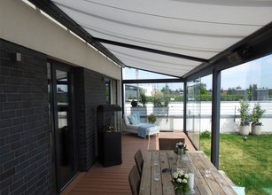 Terrassensituation mit Überdachung, Holzterrasse, Markisentuch und Glas-Schiebewänden in einer modernen Umgebung. 