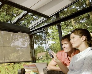 Couple utilisant une télécommande dans un espace lumineux avec des stores. Verdure visible à l'extérieur.
