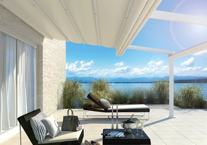 Terrassensituation mit Überdachung, Markisentuch und Blick auf Wasser und Berge, hellblauer Himmel.