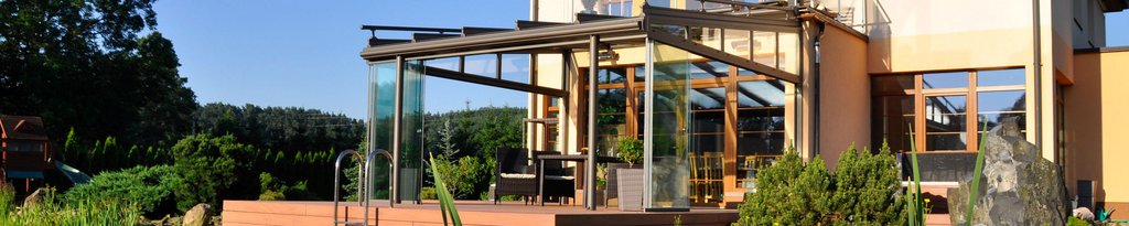 Moderne Überdachung mit Glas und Holz, umgeben von Pflanzen und einer Terrassensituation.