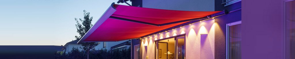 Markise in leuchtendem Pink über einer Terrassensituation, beleuchtet von warmem Licht.